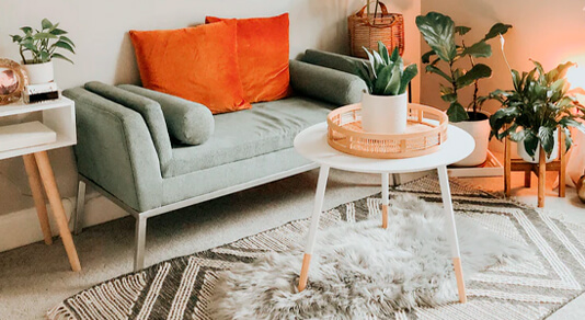 Electic interior of greens, creams and oranges showing a lot of plants and a small, round coffee table